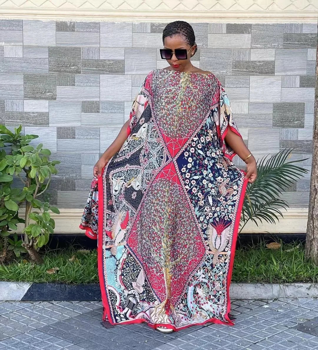 Eine Frau in einem farbenfrohen, bohemienartigen Seidendruck-Kaftan steht draußen vor einer strukturierten Wand.