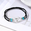 Tobillera de cuentas negras con collares de corazón de plata y cuentas turquesas, sobre fondo blanco.