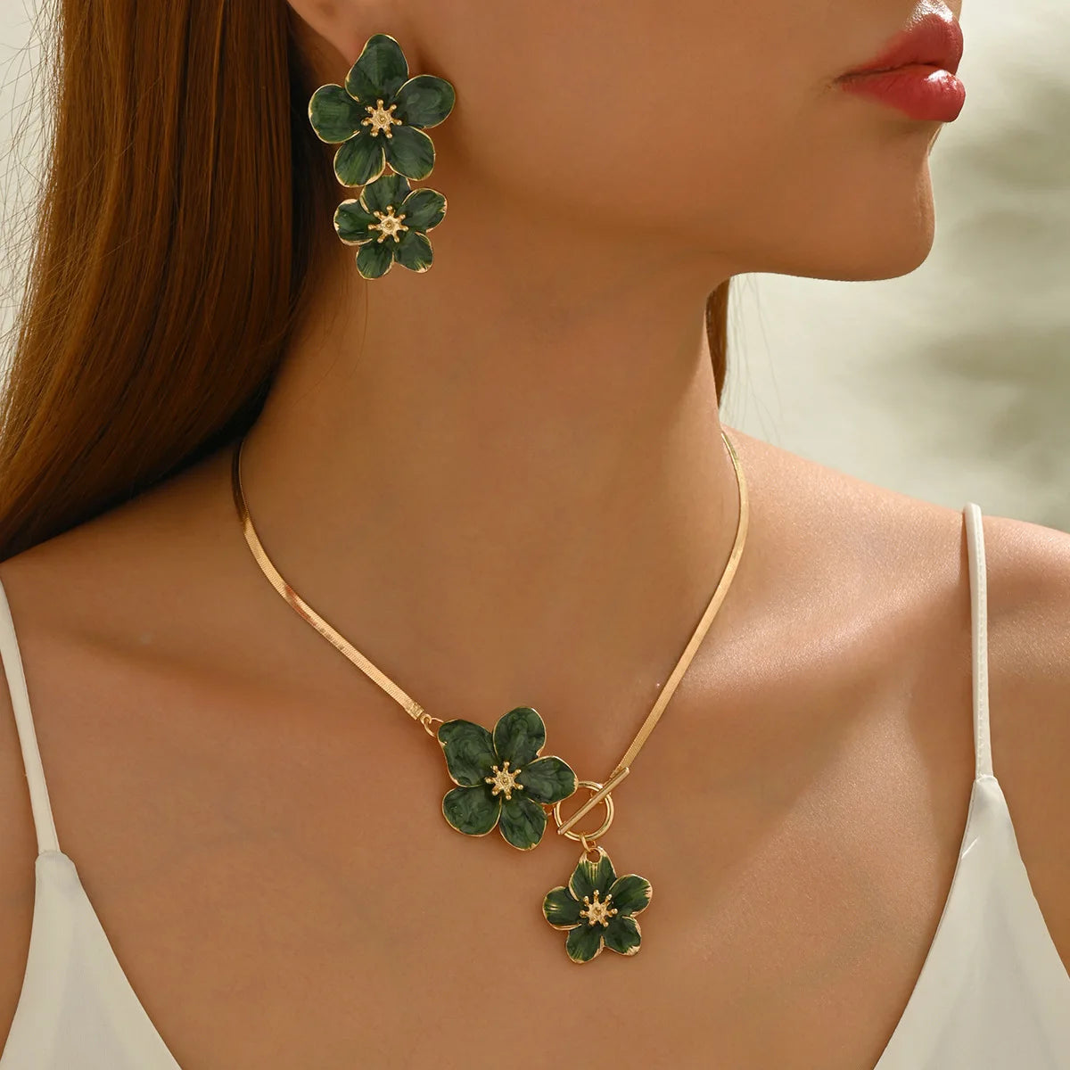 A close-up of a woman wearing a gold floral pendant necklace and matching earrings against her neck and shoulder.