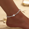 A delicate silver anklet featuring sparkling zircon stones and a pearl drop worn on a woman's ankle.
