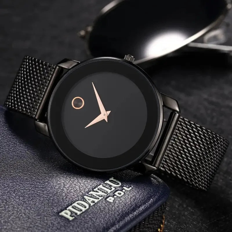 A black quartz wristwatch with a gold-toned case and a black mesh strap resting on a dark surface.