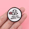A black enamel pin featuring a simple line drawing of a brain and the text Hey you dropped this