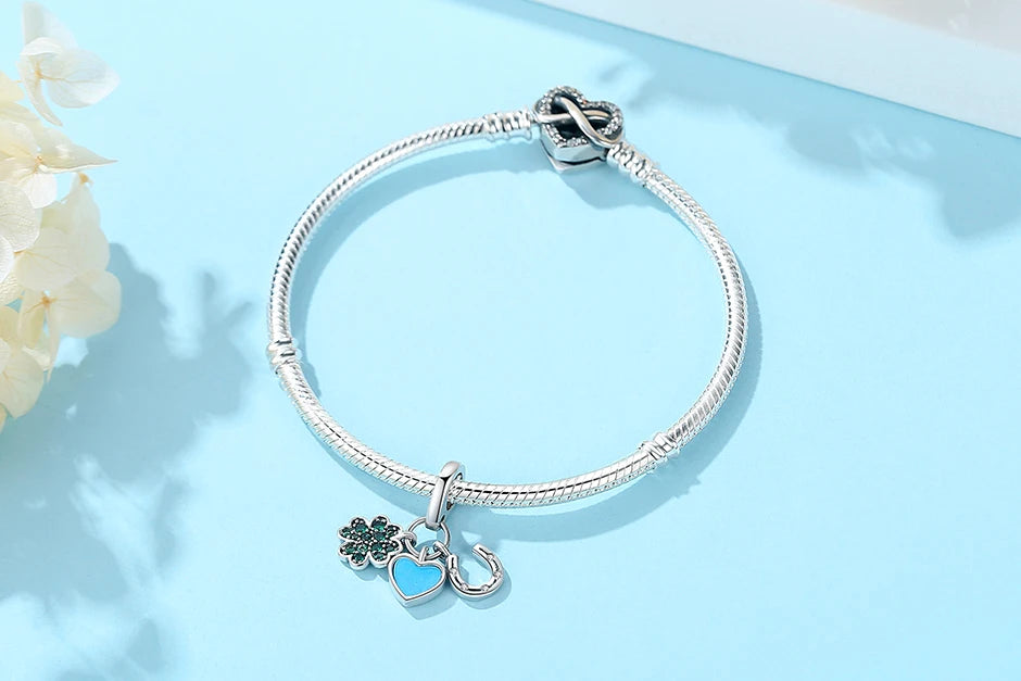 A silver bracelet featuring a family tree charm and a heart pendant on a light blue background.