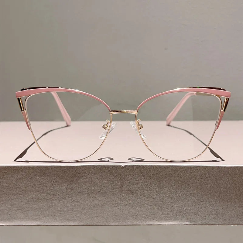 Un par de gafas de computadora con forma de ojo de gato metálicas rosas sobre una caja de color claro.