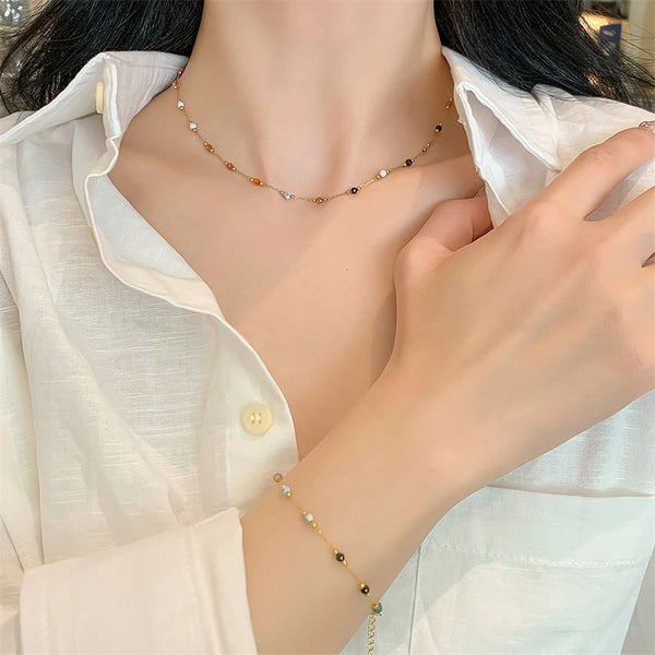 A close-up of a woman wearing a delicate gold beaded necklace and a matching bracelet, paired with a light colored shirt.