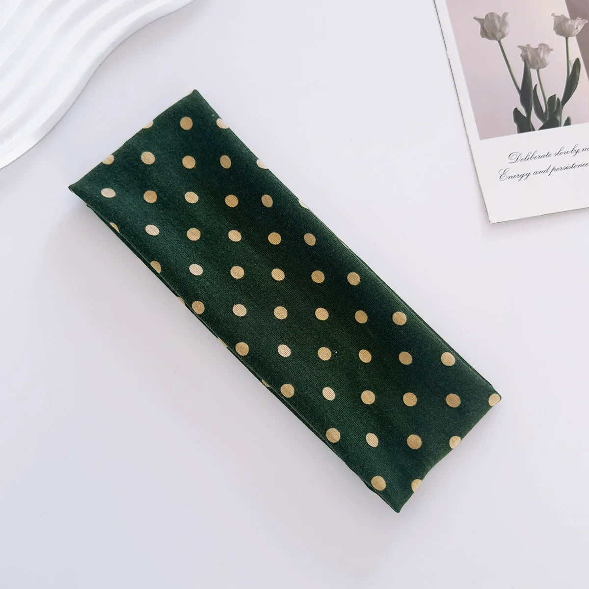 Dark green fabric hairband with gold polka dots lying on a white surface.