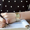 A hand is writing in a notebook next to a classic gold military style wristwatch.