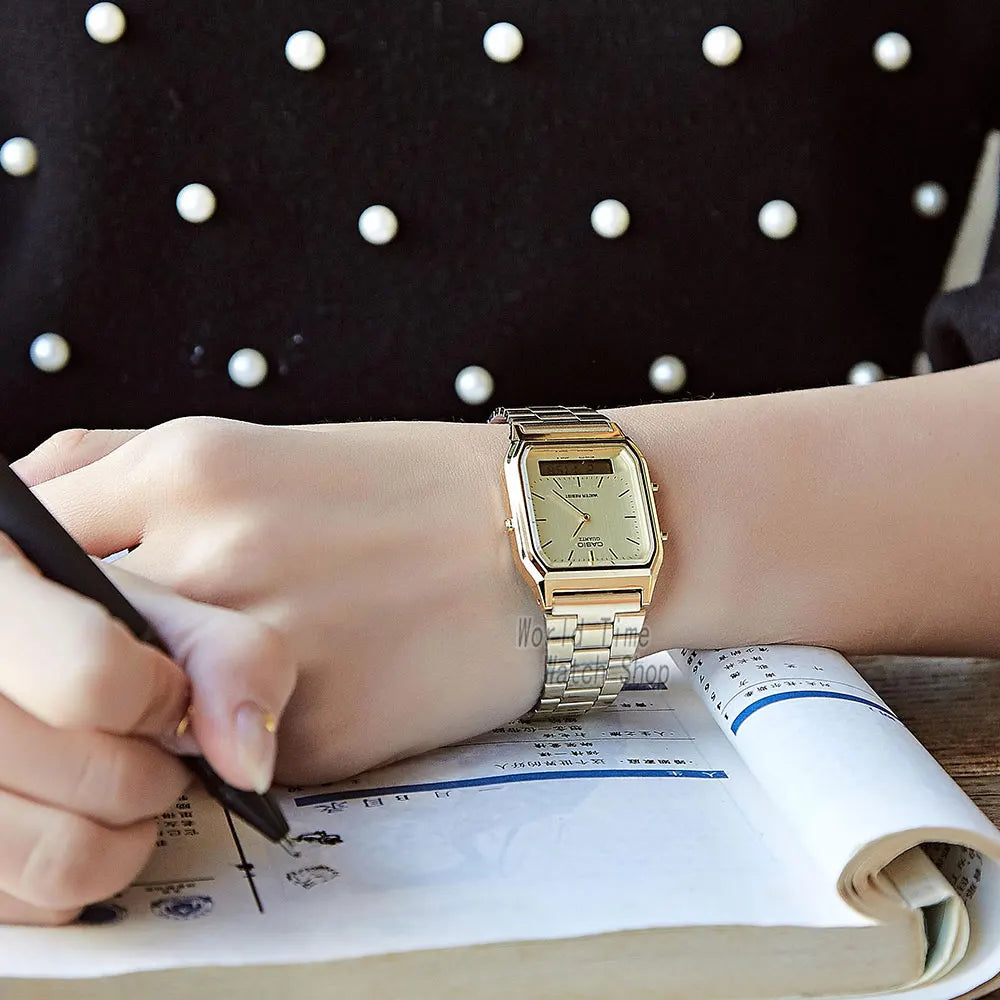 A hand is writing in a notebook next to a classic gold military style wristwatch.