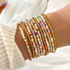 A stack of colorful beaded bangles worn on a wrist, featuring various shades of pink, yellow, and white.