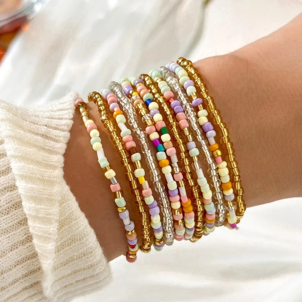 A stack of colorful beaded bangles worn on a wrist, featuring various shades of pink, yellow, and white.
