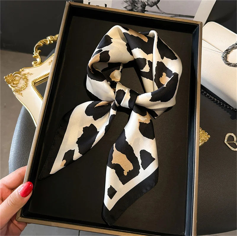 A black and white leopard print silk scarf tied in a bow displayed in a square wooden frame.