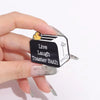 A hand holds a black enamel pin featuring a duck and the text Live Laugh Toaster Bath