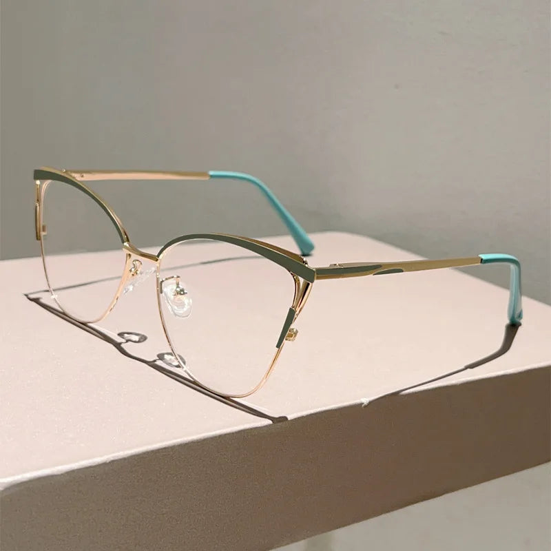 Un par de gafas de computadora con montura metálica dorada y detalles azul claro, sobre una superficie blanca.