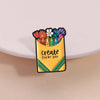 A yellow enamel brooch featuring a colorful arrangement of flowers and the text create every day.