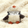 Un peluche de pingüino esponjoso con detalles naranjas, apoyado sobre una superficie blanca texturizada mostrando una abertur