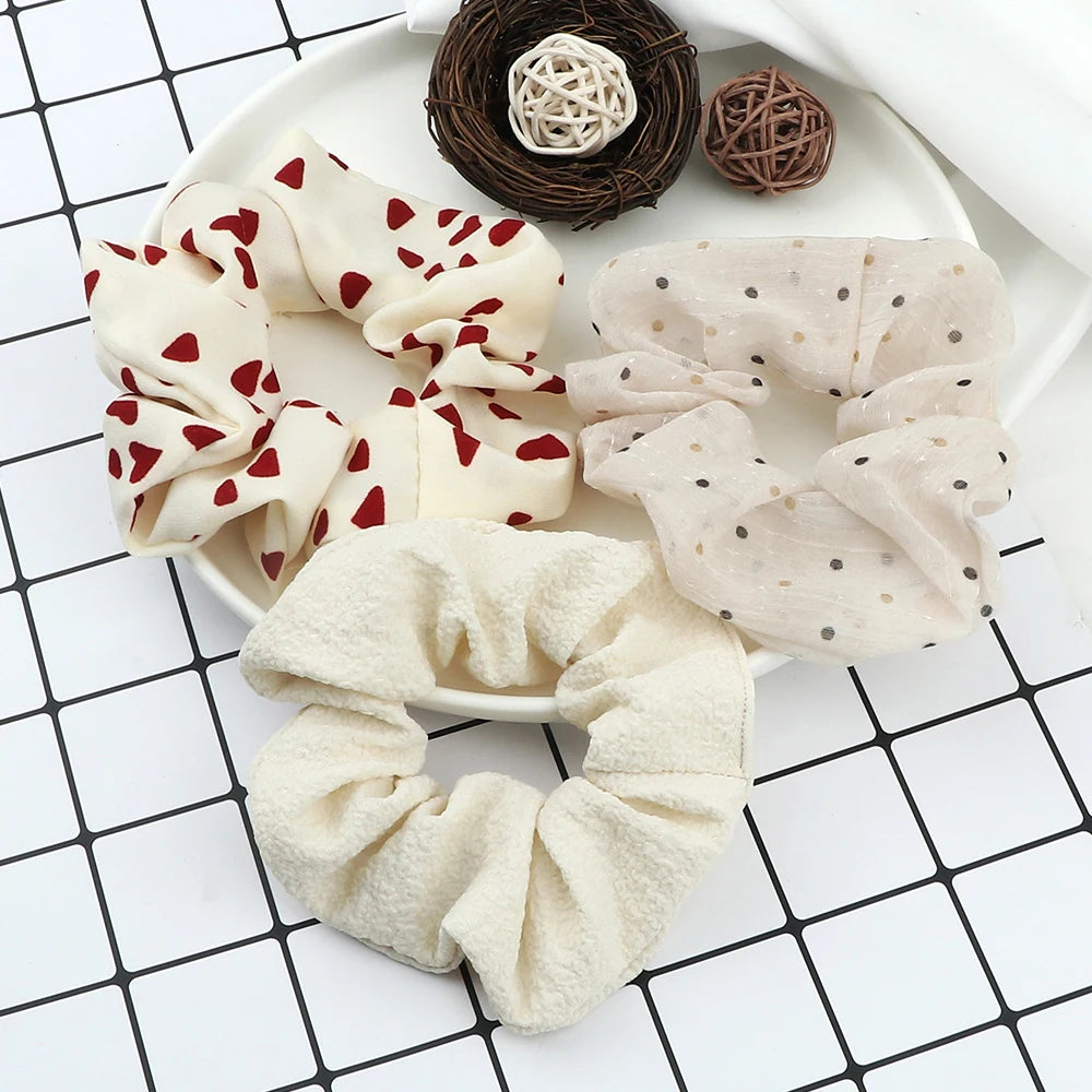 A set of three knitted hair scrunchie headbands in cream and beige colors with various patterns displayed on a white plate.