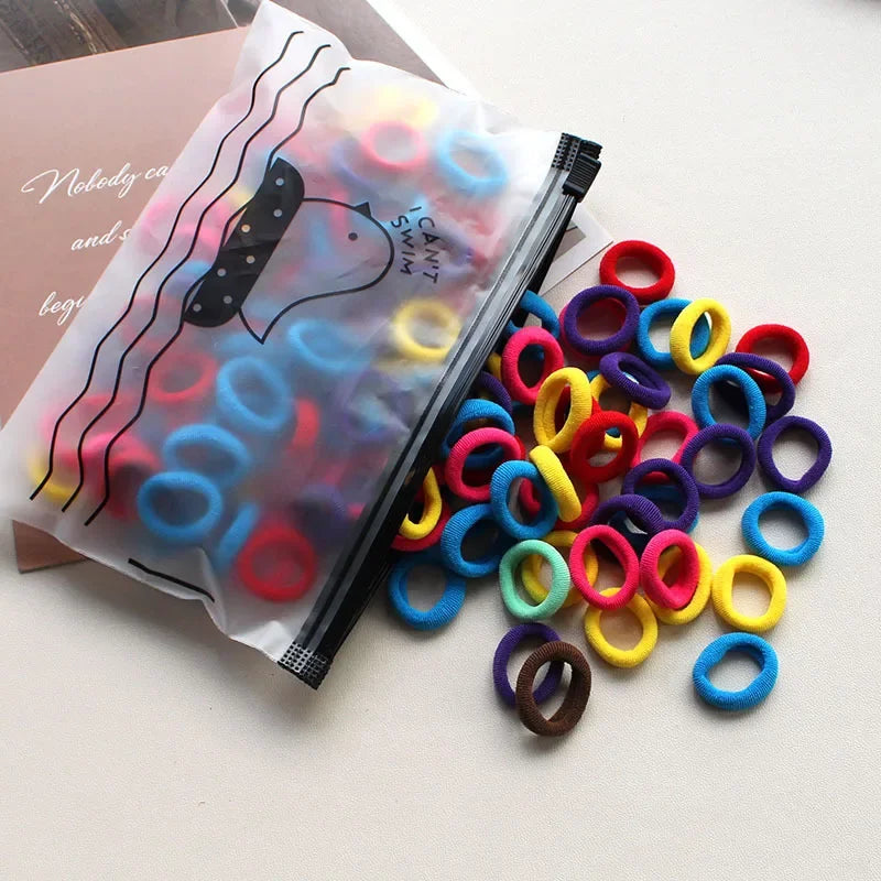 A collection of colorful elastic hair bands in various colors and sizes is displayed next to a clear plastic bag.
