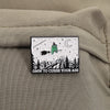 An enamel pin featuring a green frog wizard with a broom and a crescent moon over a snowy mountain landscape.