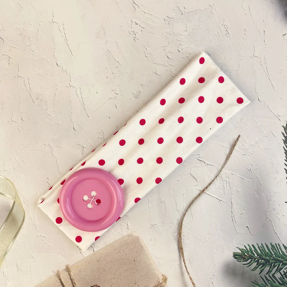 A pink polka dot fabric headband lying on a light surface next to a natural twine and green foliage.