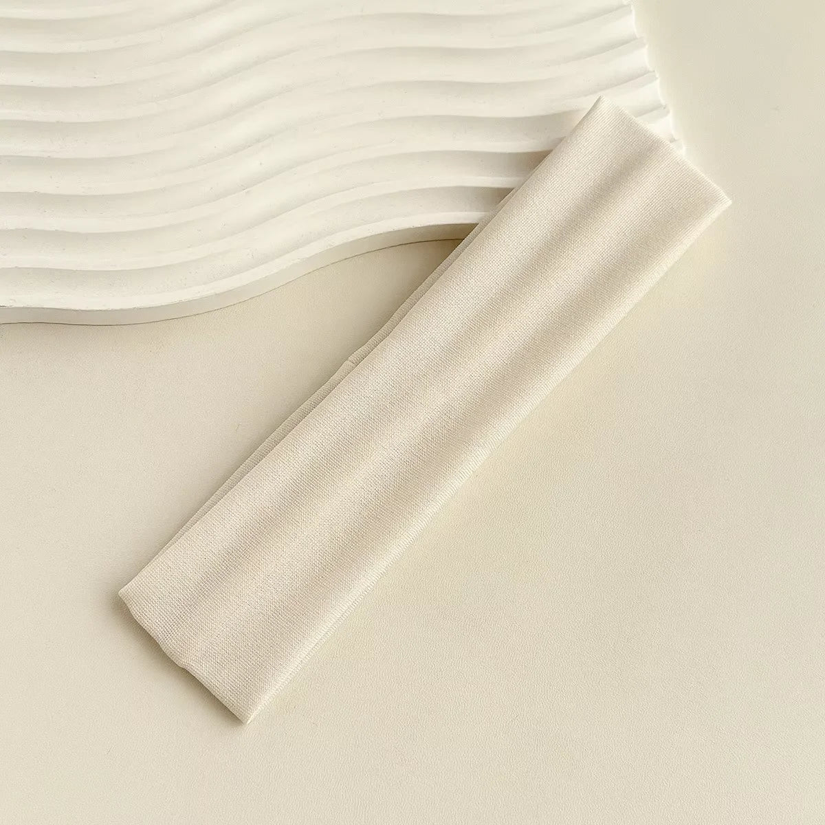 A beige fabric headband is shown next to a wavy white background.