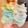 A hand holds a set of pastel green and white flower bow hair ties for girls.