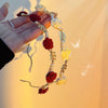 A hand holds an elegant rose vine headband hair accessory featuring red and yellow roses and pearls.