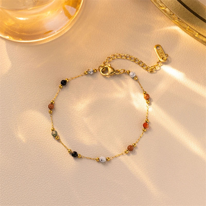 A gold-toned beaded jewelry set featuring various colored stones and a clasp, displayed on a light background.