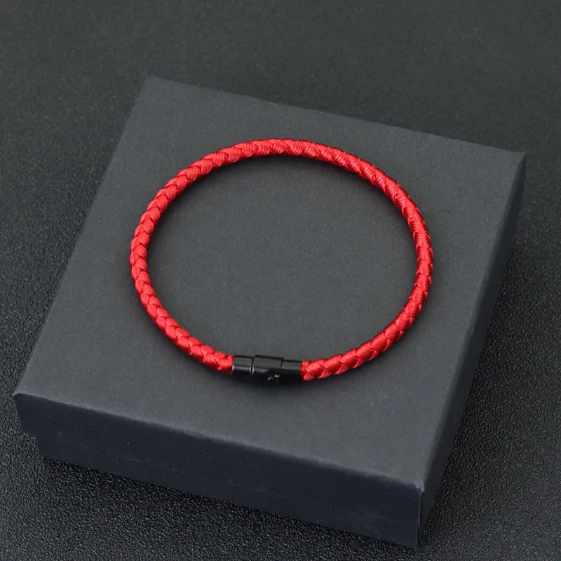 A red thread charm bracelet is displayed on a dark gray box.