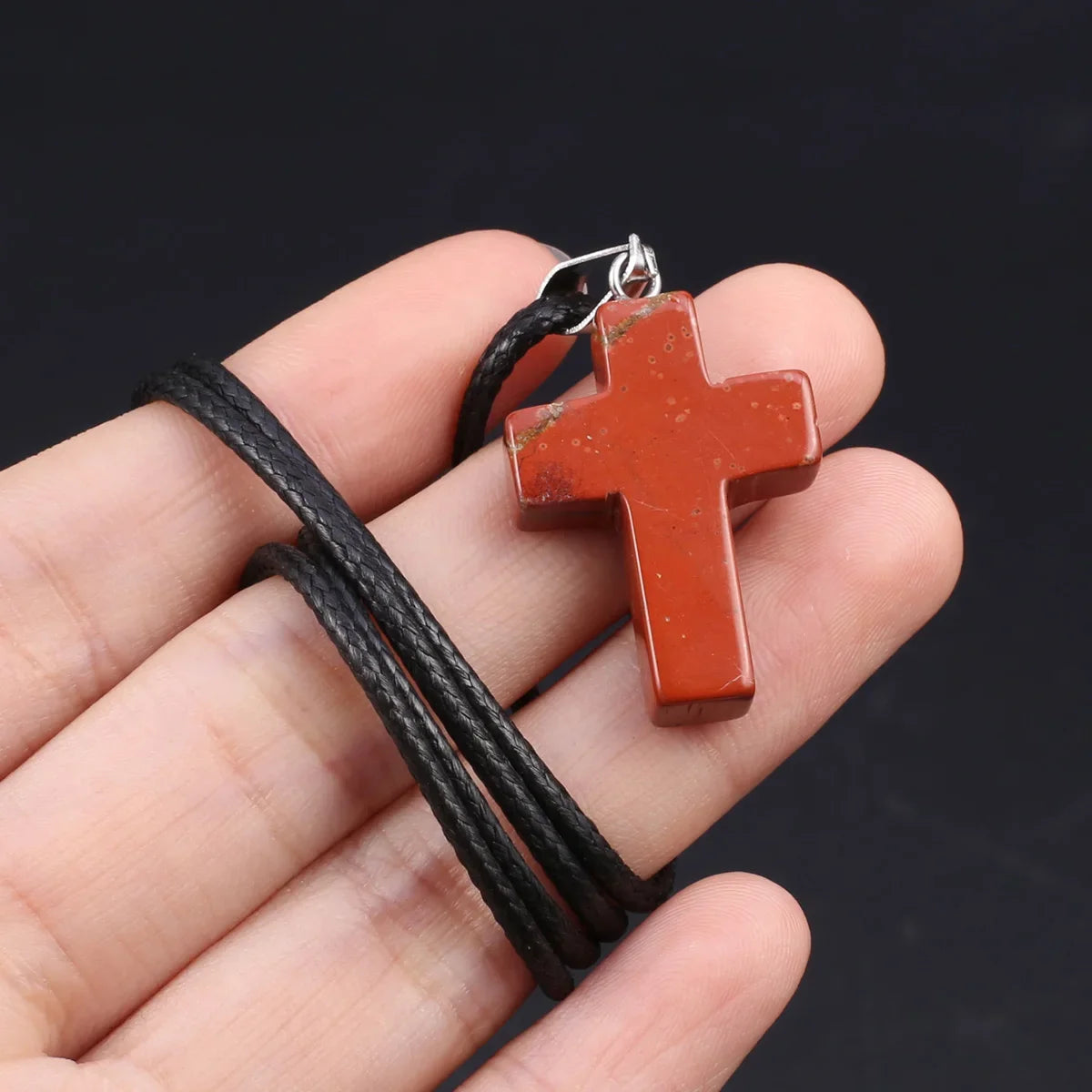 Eine Hand hält eine rötlich-braune Tigerauge-Agat-Kreuz-Anhänger-Kette vor dunklem Hintergrund.