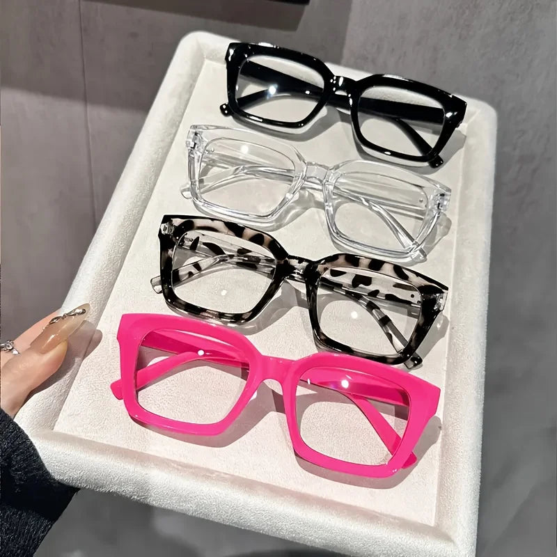 A collection of various eyeglasses, including black, clear, and pink frames, displayed on a white tray.