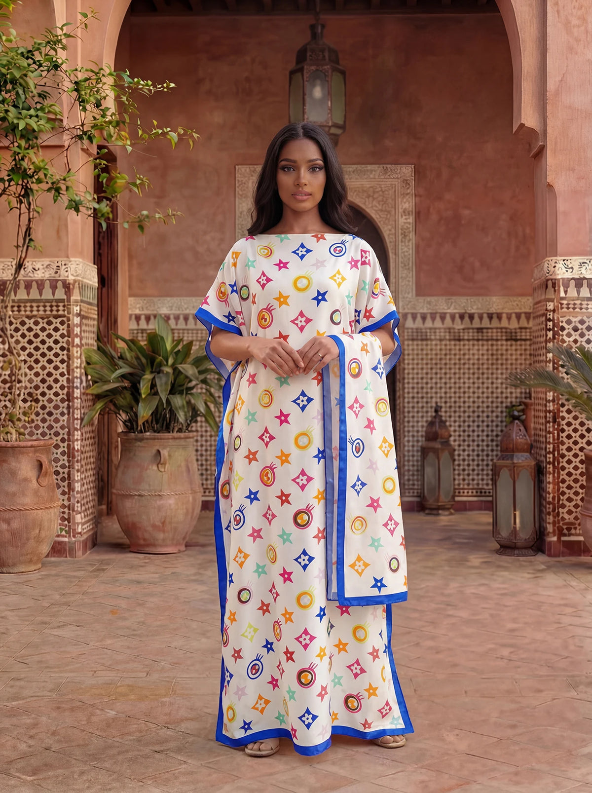A woman wearing a floral print satin maxi shawl in white and blue tones stands in an arched outdoor setting.