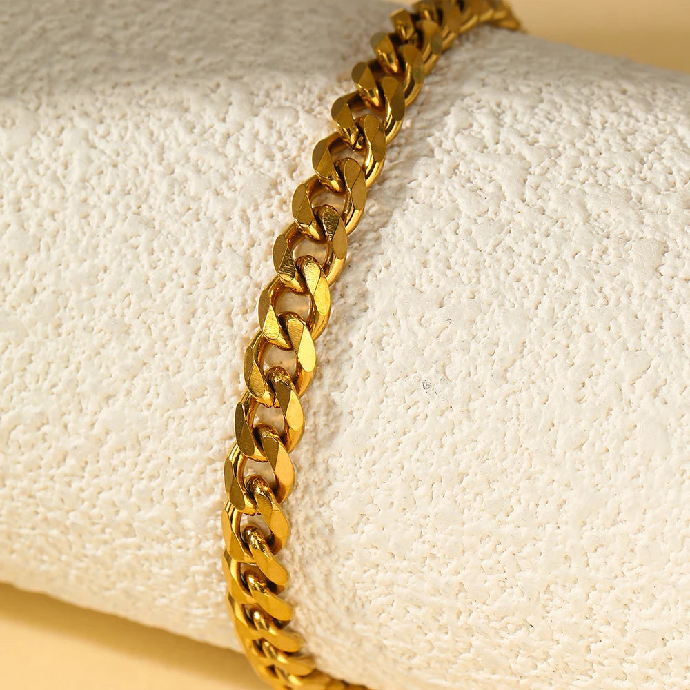A close-up of a gold-toned multi-chain stainless steel anklet worn on a wrist against a white background.