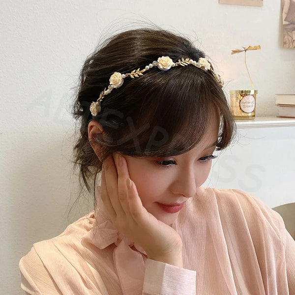 A woman wearing an elegant rose vine headband hair accessory, looking down and touching her face.
