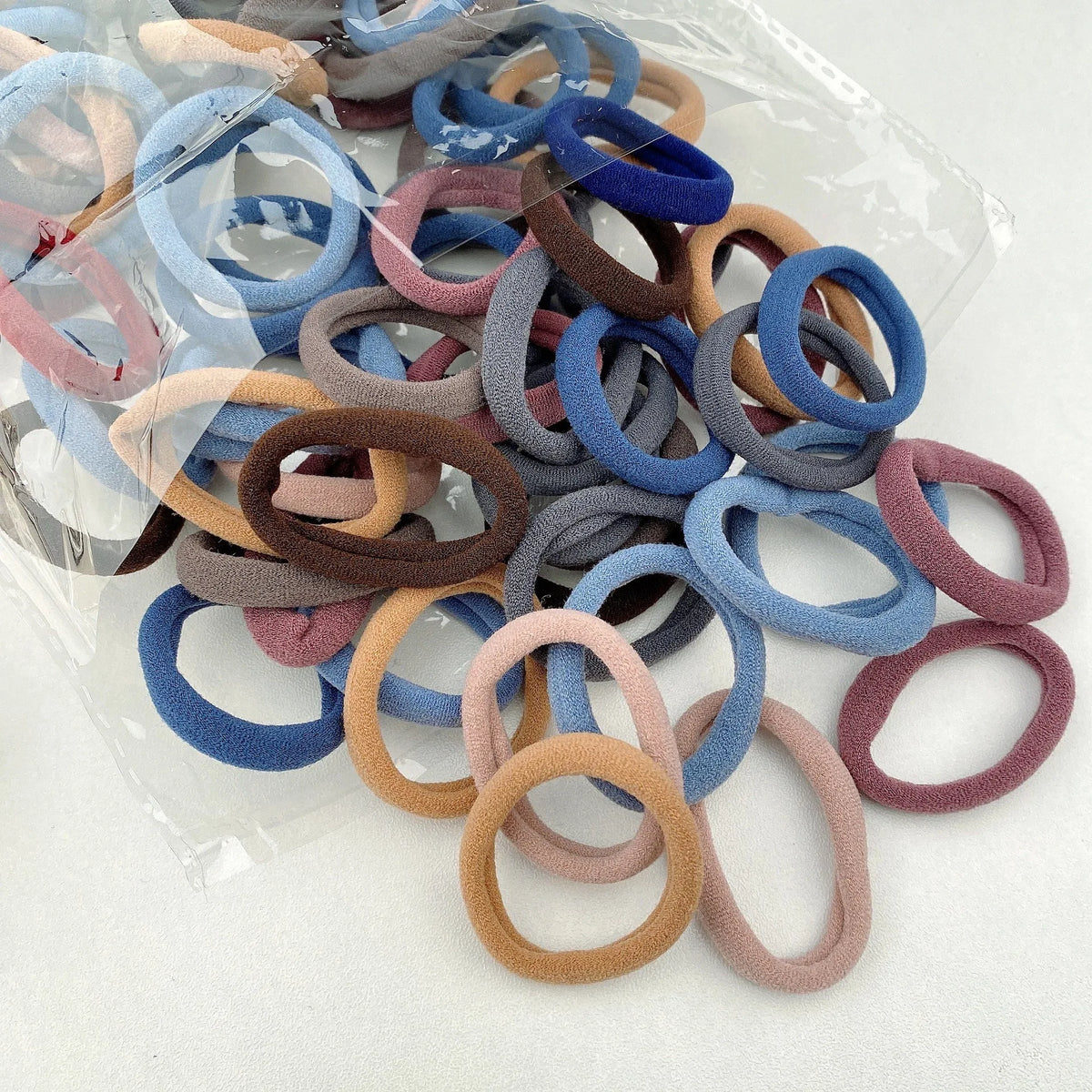 A collection of colorful elastic hair bands in various shades of blue, pink, and brown are displayed in a clear plastic bag.