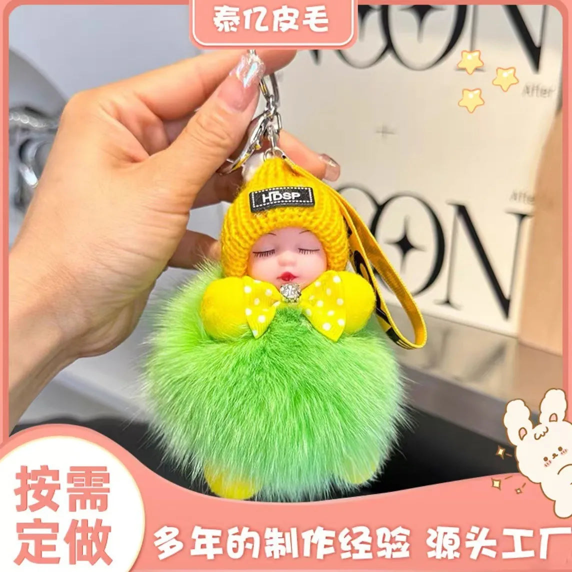 A hand holds a yellow and green plush doll with a gold keychain, featuring a cartoon face.