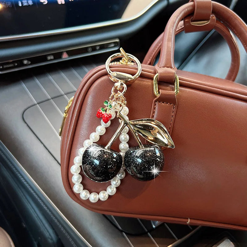 A brown leather handbag with a gold key chain decoration featuring pearl beads and a shiny black cherry charm.