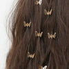 A close-up of dark brown hair adorned with ten small gold metal butterfly hair clips.