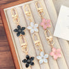 Llavero floral tono dorado con pétalos rosas y blancos, apto para llaves y bolsos.