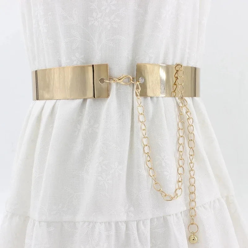 Une chaîne de ceinture métallique couleur or est présentée sur un tissu de robe blanche.