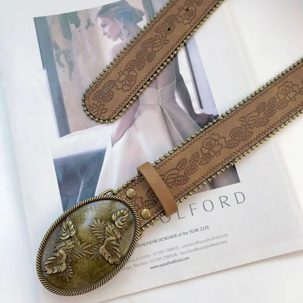 A close-up of a vintage PU leather boho western belt with an oval buckle and detailed stitching on a white background.