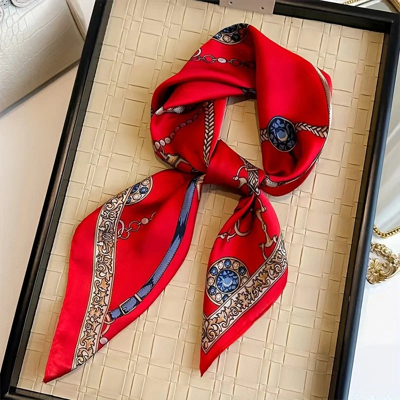 A vibrant red silk scarf tied in a knot, featuring intricate gold and blue embroidery, displayed in a black frame.