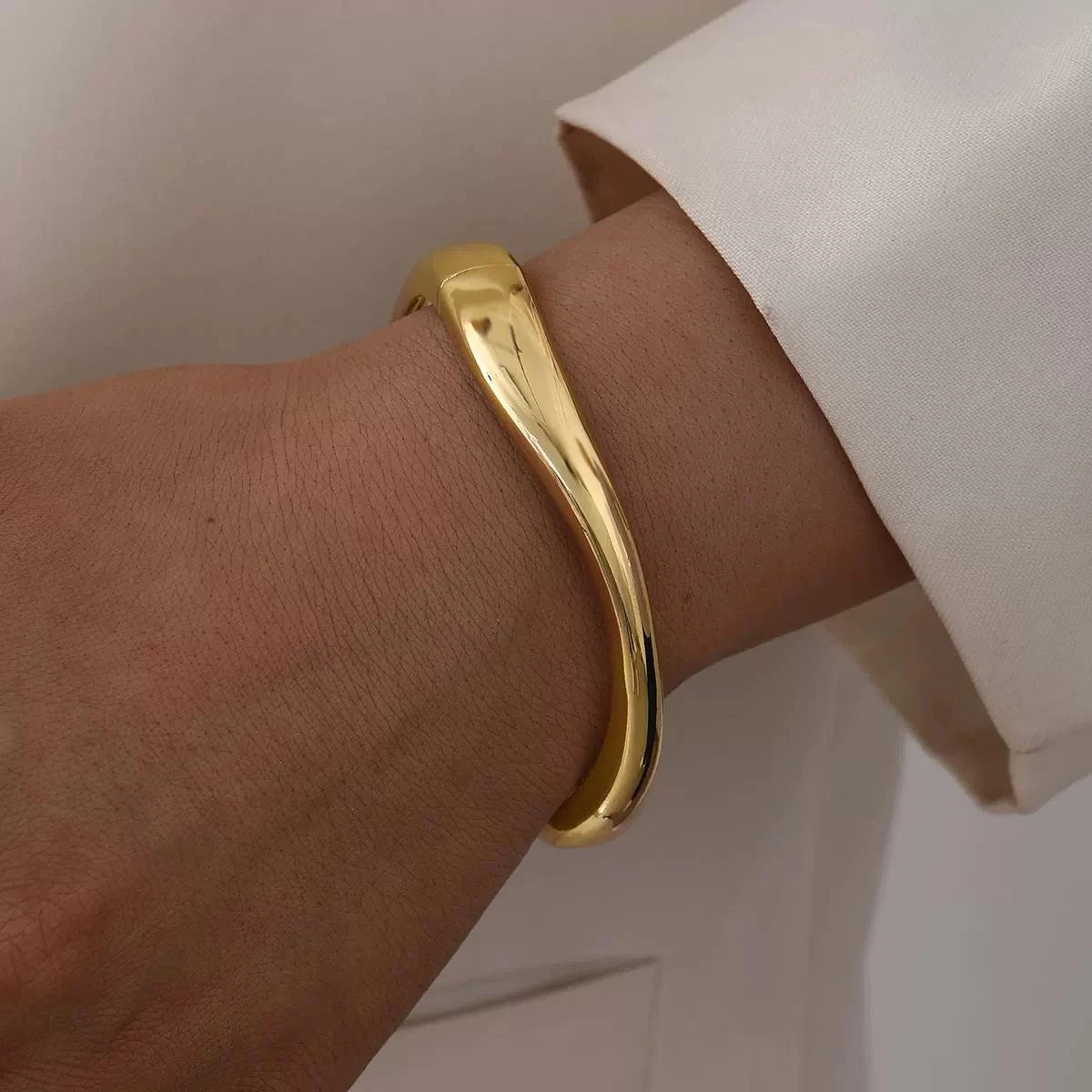 A close-up of a gold chunky cuff bangle bracelet worn on a wrist against a white background.