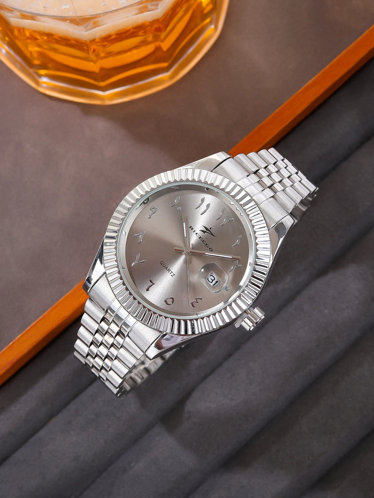 A silver luxury quartz men's wristwatch with a metal bracelet and date display resting on a gray fabric.