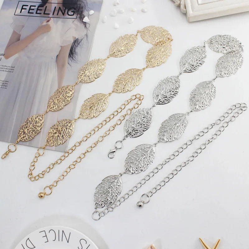 Colección de cadenas y cinturones metálicos en forma de hoja de oro y plata, exhibidos sobre una superficie blanca.