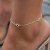 A close-up of a gold plated dainty ankle bracelet with small blue gemstones on a person's skin.