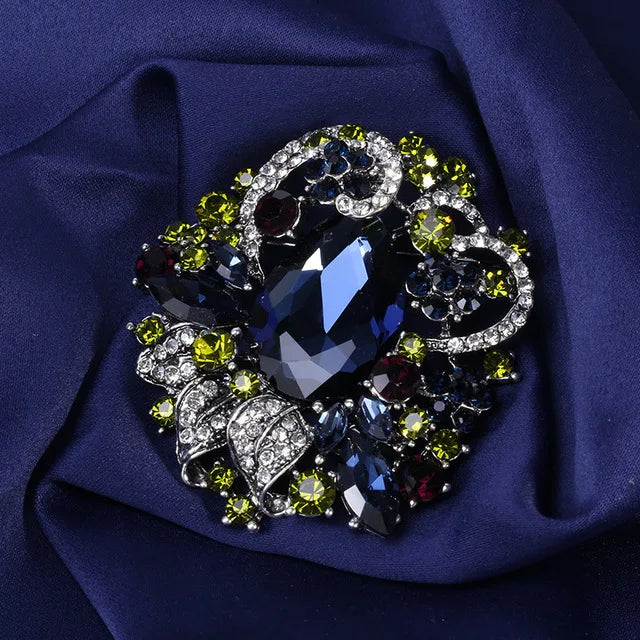 Broche florale en cristal élégante avec des gemmes bleu foncé et vert sur un tissu bleu profond.