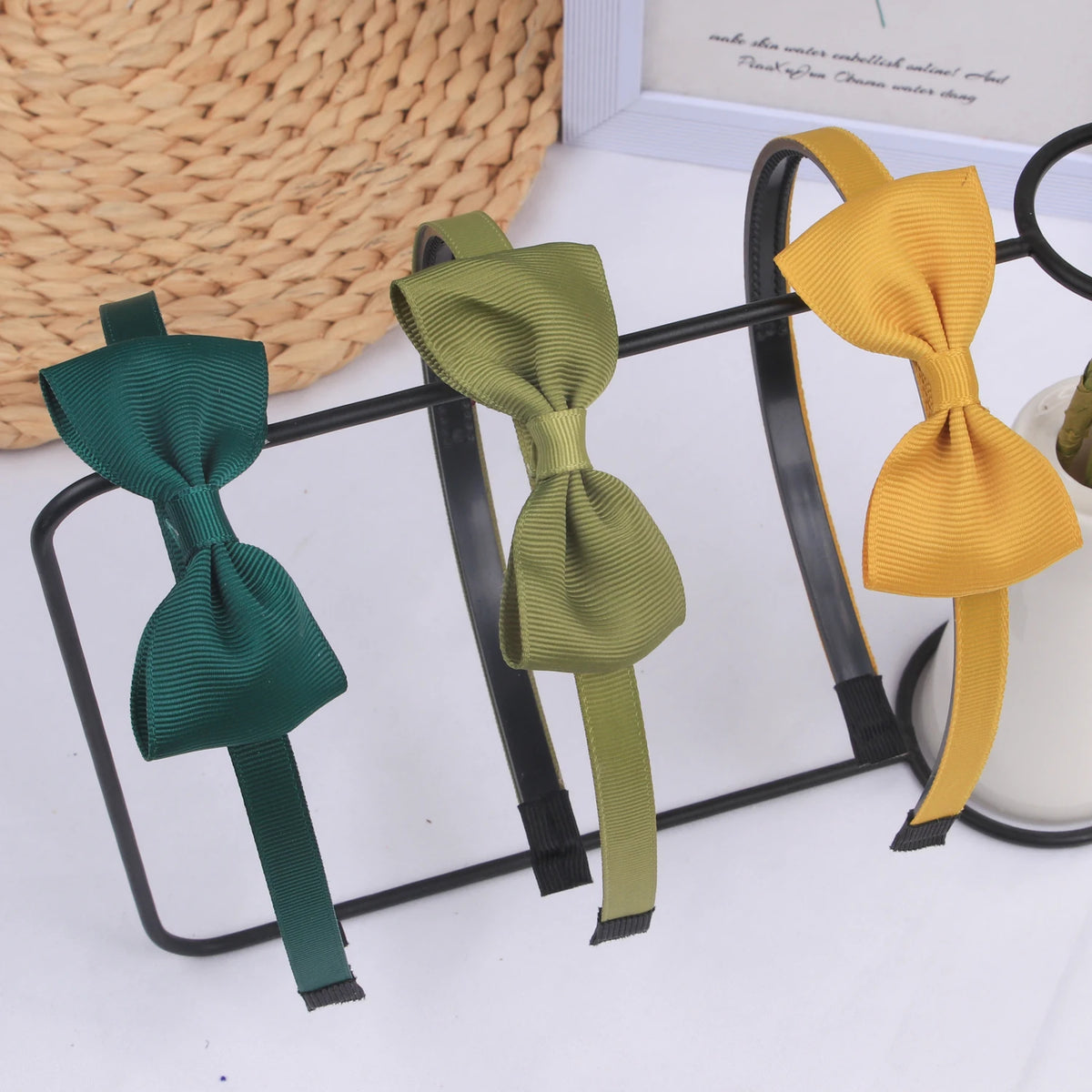 Three decorative grosgrain ribbon hair bows in shades of dark green, olive green, and mustard yellow displayed on a black wir
