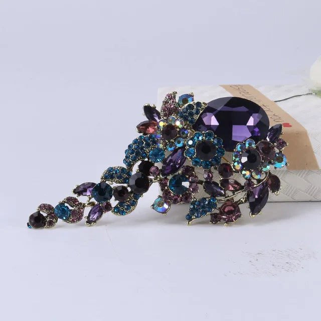 Broche florale en cristal élégante avec des gemmes violettes et bleues sur une monture dorée.