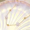 Collier délicat en or avec de petites perles blanches, exposé sur une surface rose pâle.