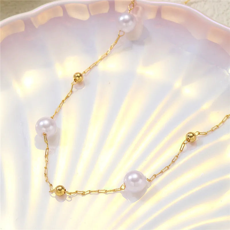 Collier délicat en or avec de petites perles blanches, exposé sur une surface rose pâle.